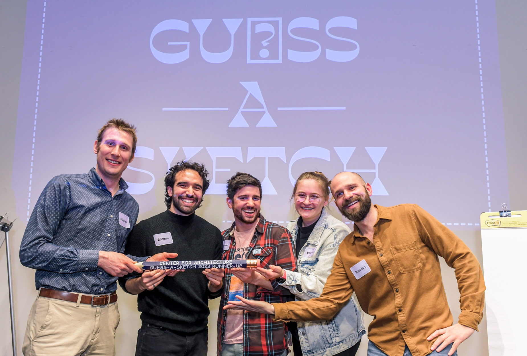 Guess-A-Sketch winners standing on stage in front of the logo.