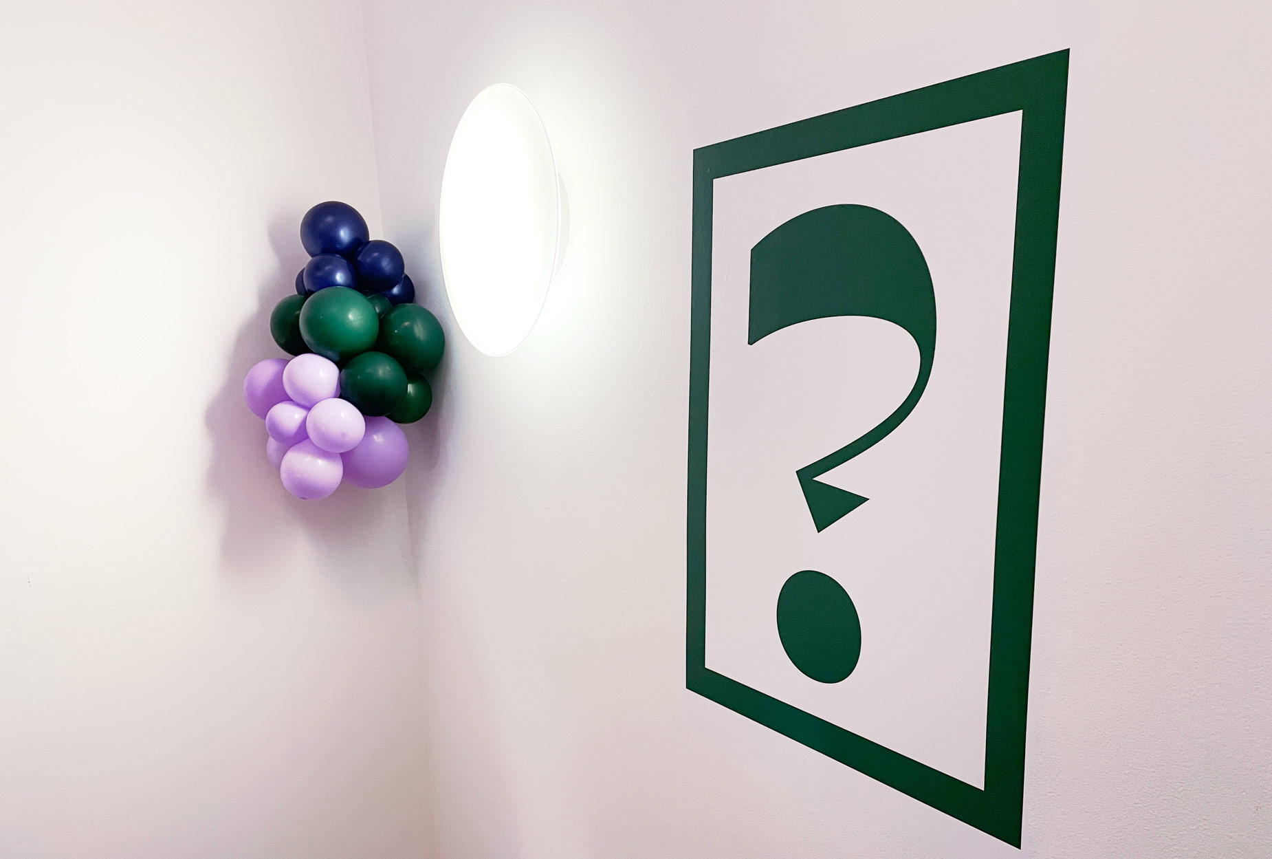 Question mark glyph and balloon clusters in brand color palette decorating the space